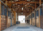 Sunlit center aisle of the GreenAcres barn lined with open box stalls