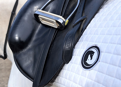 Close-up of an English saddle resting on a white pad embroidered with the GreenAcres horse-head crest